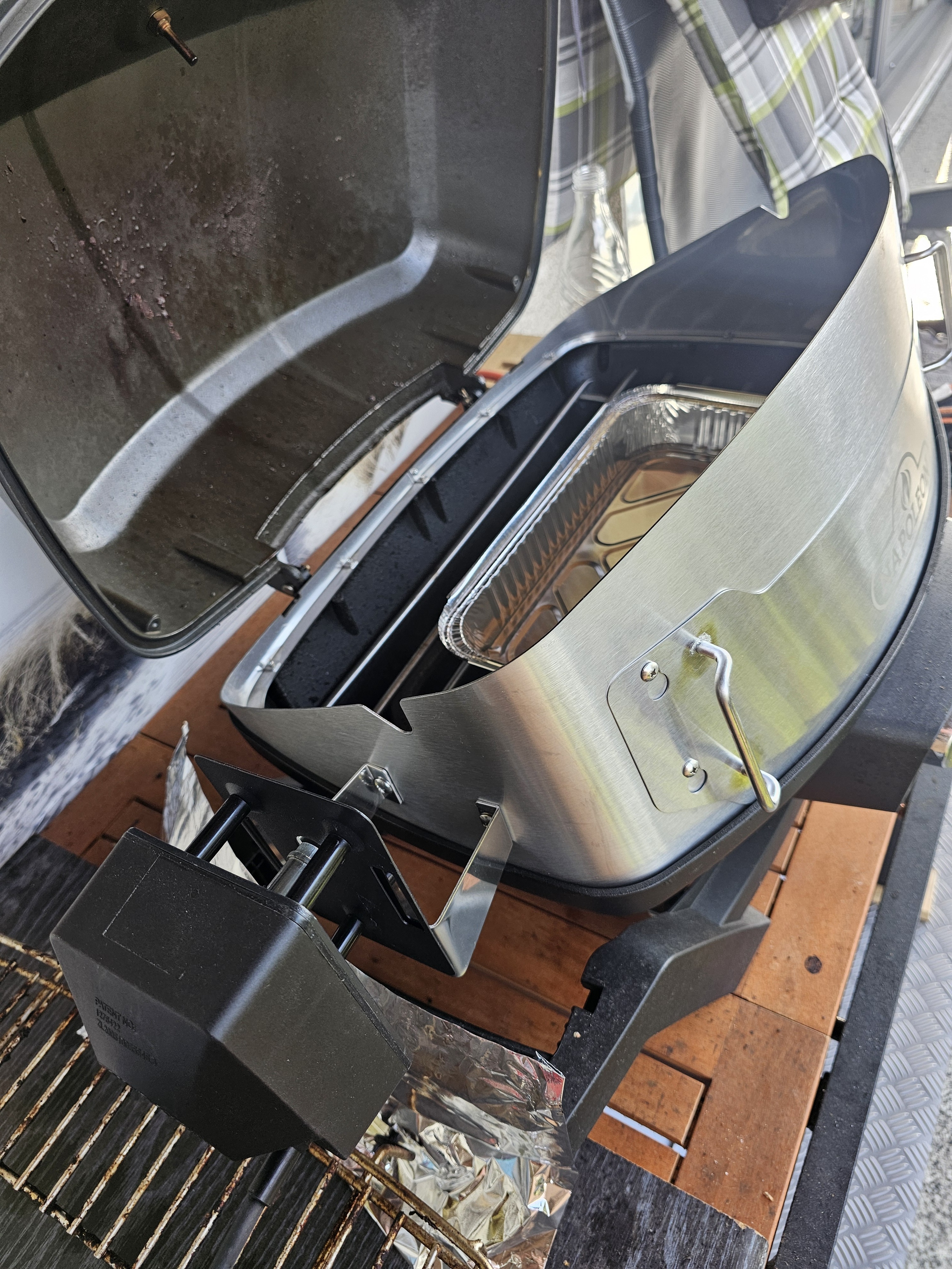 Ein offener Napoleon Grill mit silbernem Gehäuse, einer innenliegenden Aluminiumschale und einem schwarzen Motor für den Drehspieß.