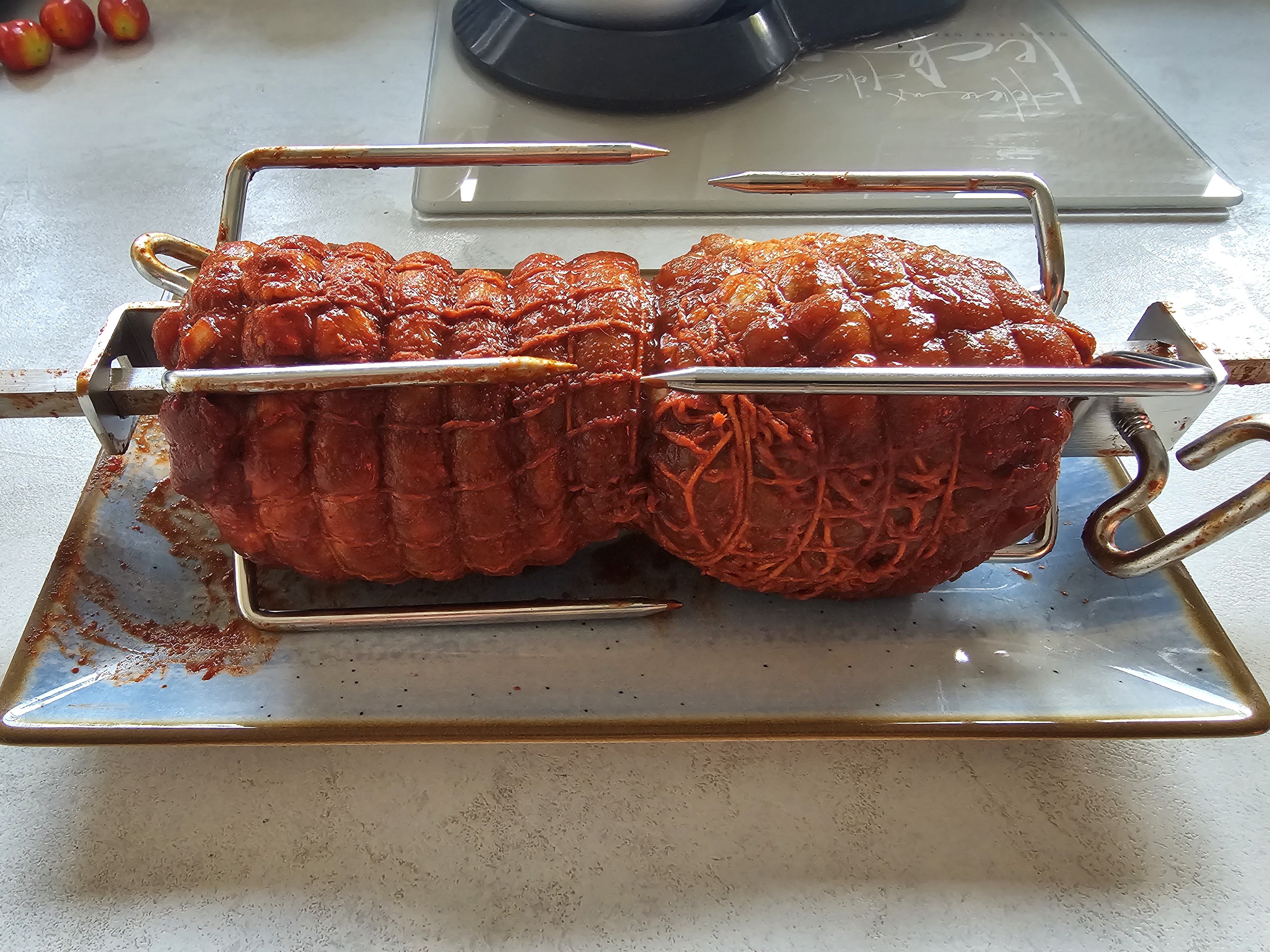 Zwei Spießbratenstücke auf einem Spieß mit Metallhalterung auf einer rechteckigen Platte